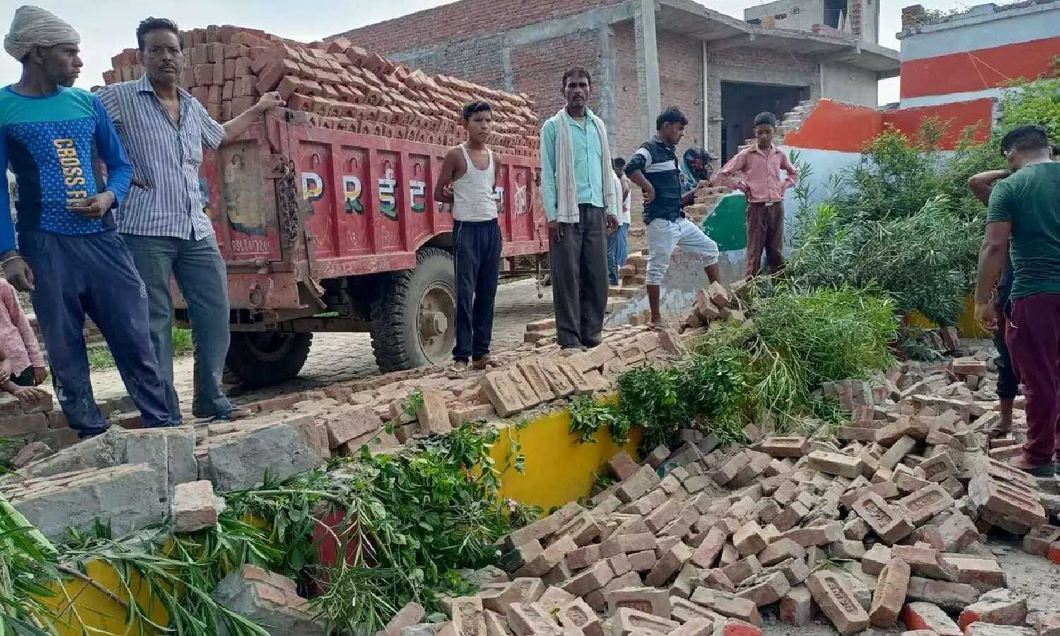 ट्रैक्टर की टक्कर से टूटी स्कूल की दीवाल देखते ग्रामीण